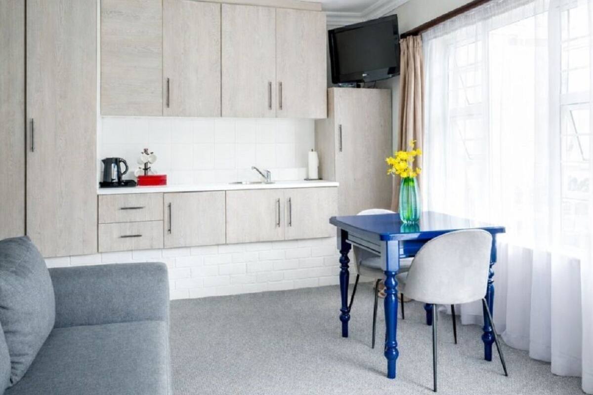 A modern kitchen with light wood cabinets, a white countertop, and a dining table with chairs.