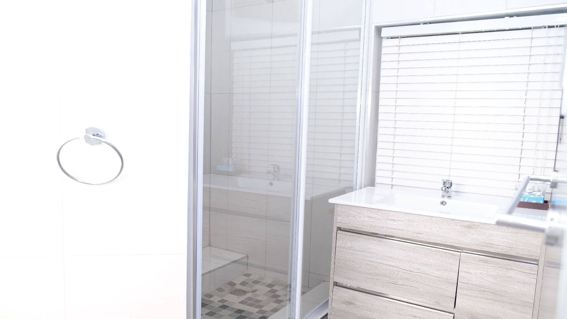 Un baño con cabina de ducha de vidrio, un lavamanos blanco con tocador de madera y un aro para toallas en la pared.