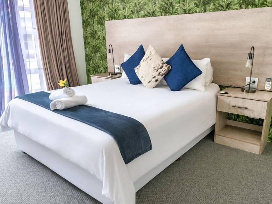 Une chambre d’hôtel avec un lit, une table de chevet, une lampe et une vue sur la verdure.