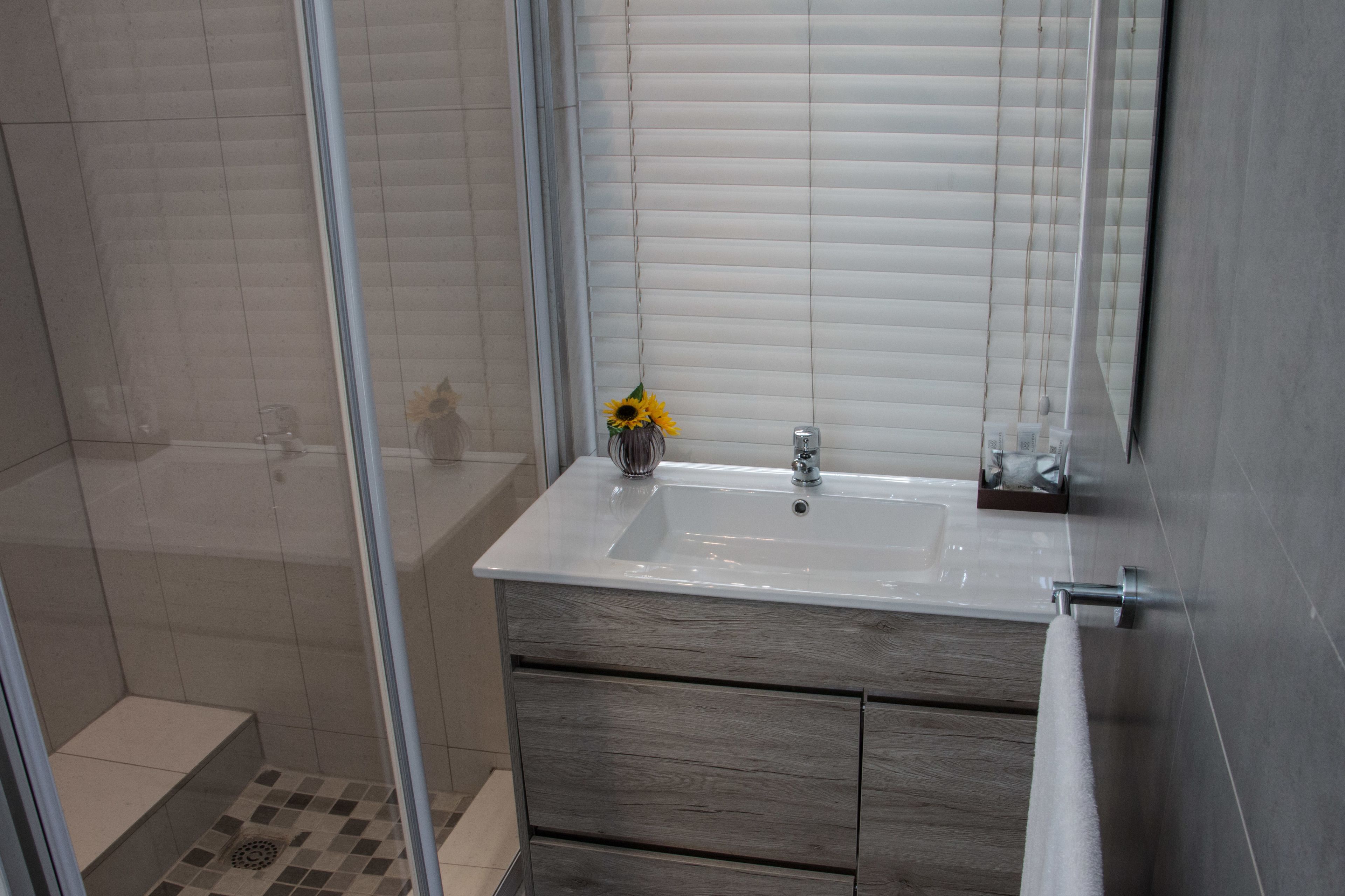 A modern bathroom with a glass shower enclosure, a white sink with a vase of sunflowers, and wooden cabinetry.