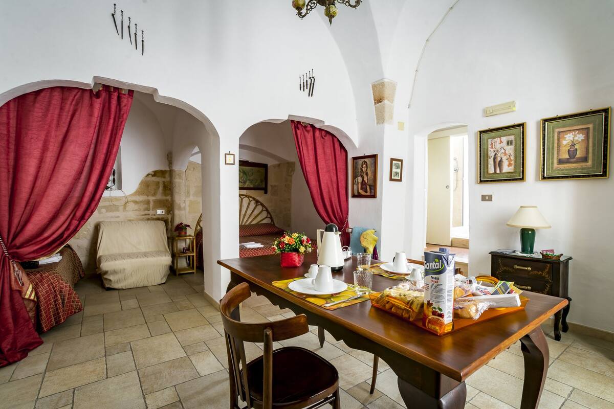 Un comedor con una mesa de madera dispuesta para dos personas, un sofá y una cama al fondo.