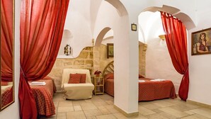 Una habitación con dos camas, cortinas rojas, un sofá y una pared de piedra.