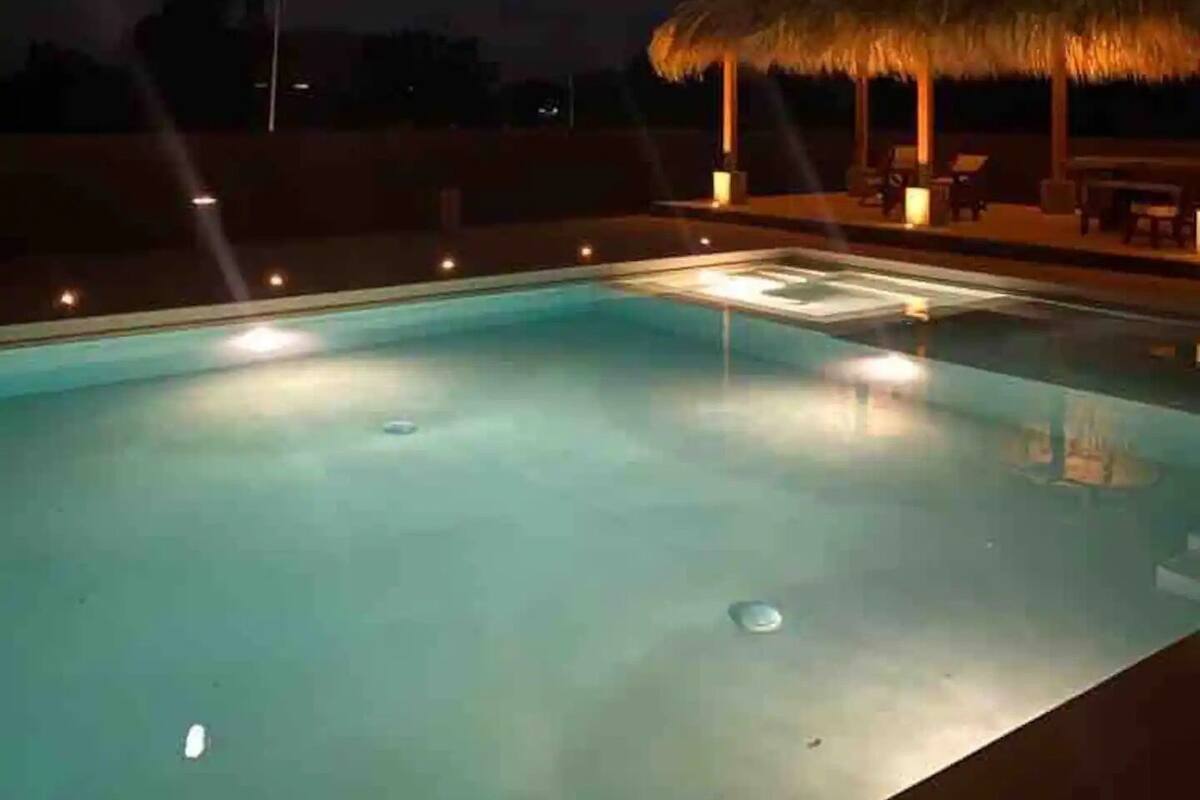 Una piscina con techo de paja e iluminación ambiental.