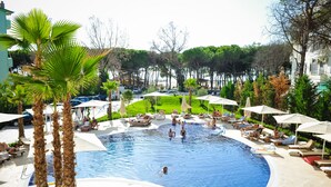 A swimming pool with lounge chairs and umbrellas, surrounded by palm trees and a grassy area.