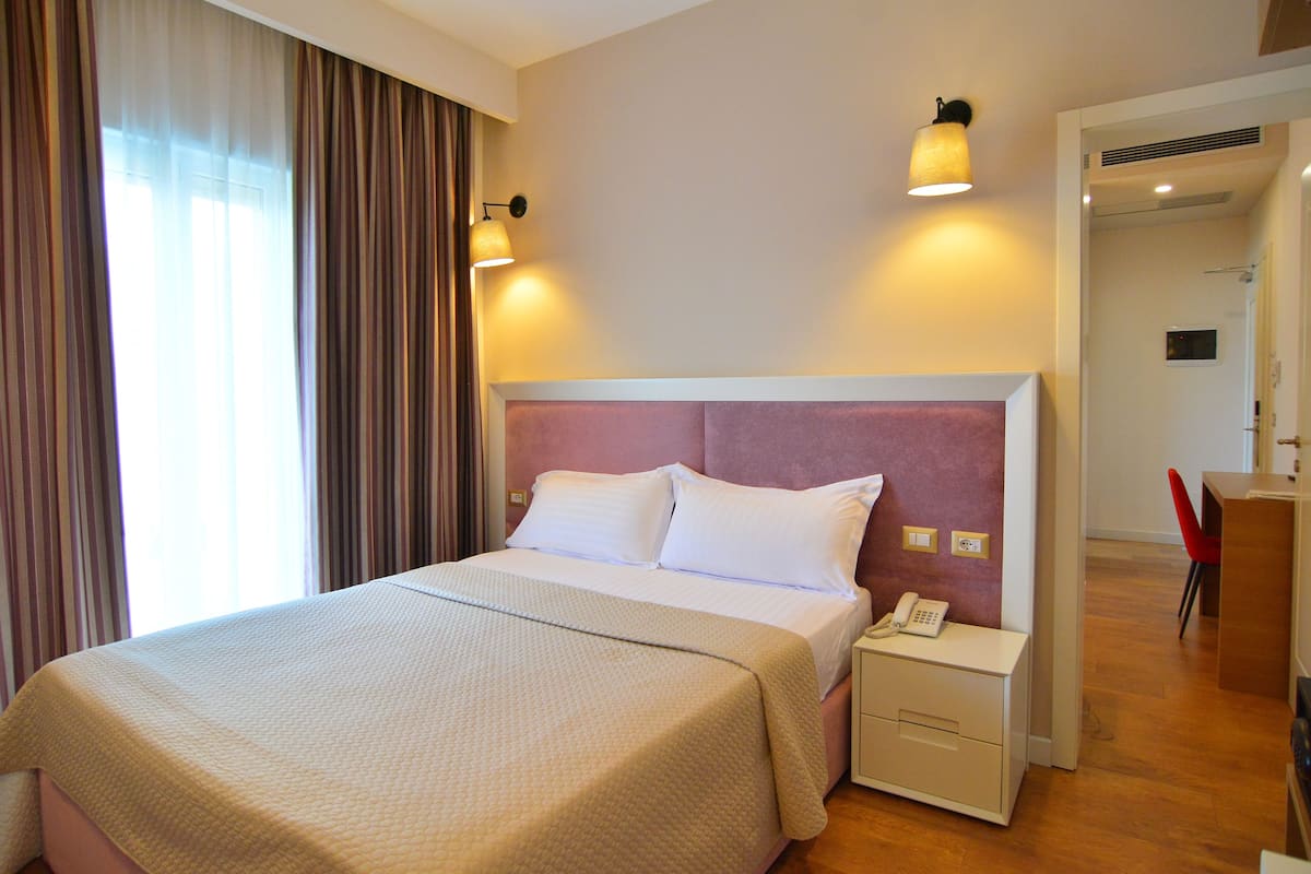 A hotel room with a bed, bedside lamp, nightstand, and a telephone.
