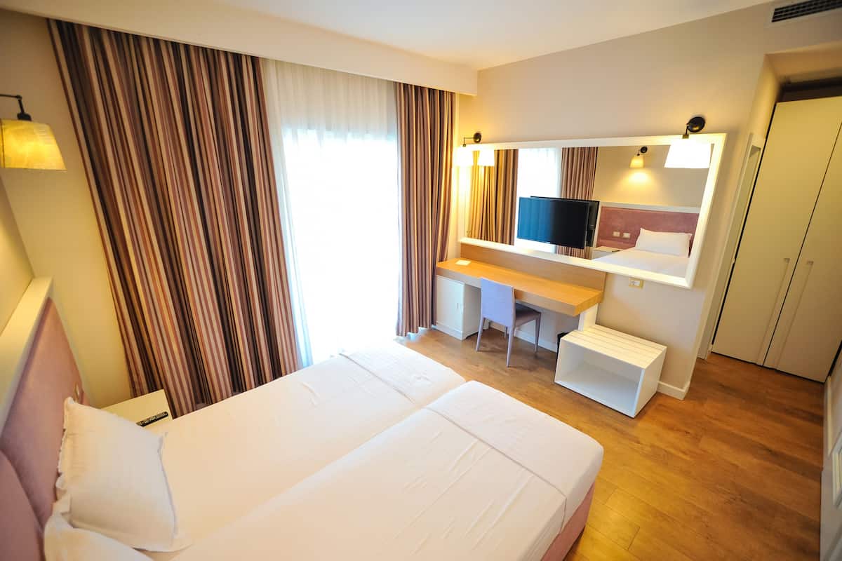 A hotel room with a large bed, a desk, a chair, a television, and a wardrobe.
