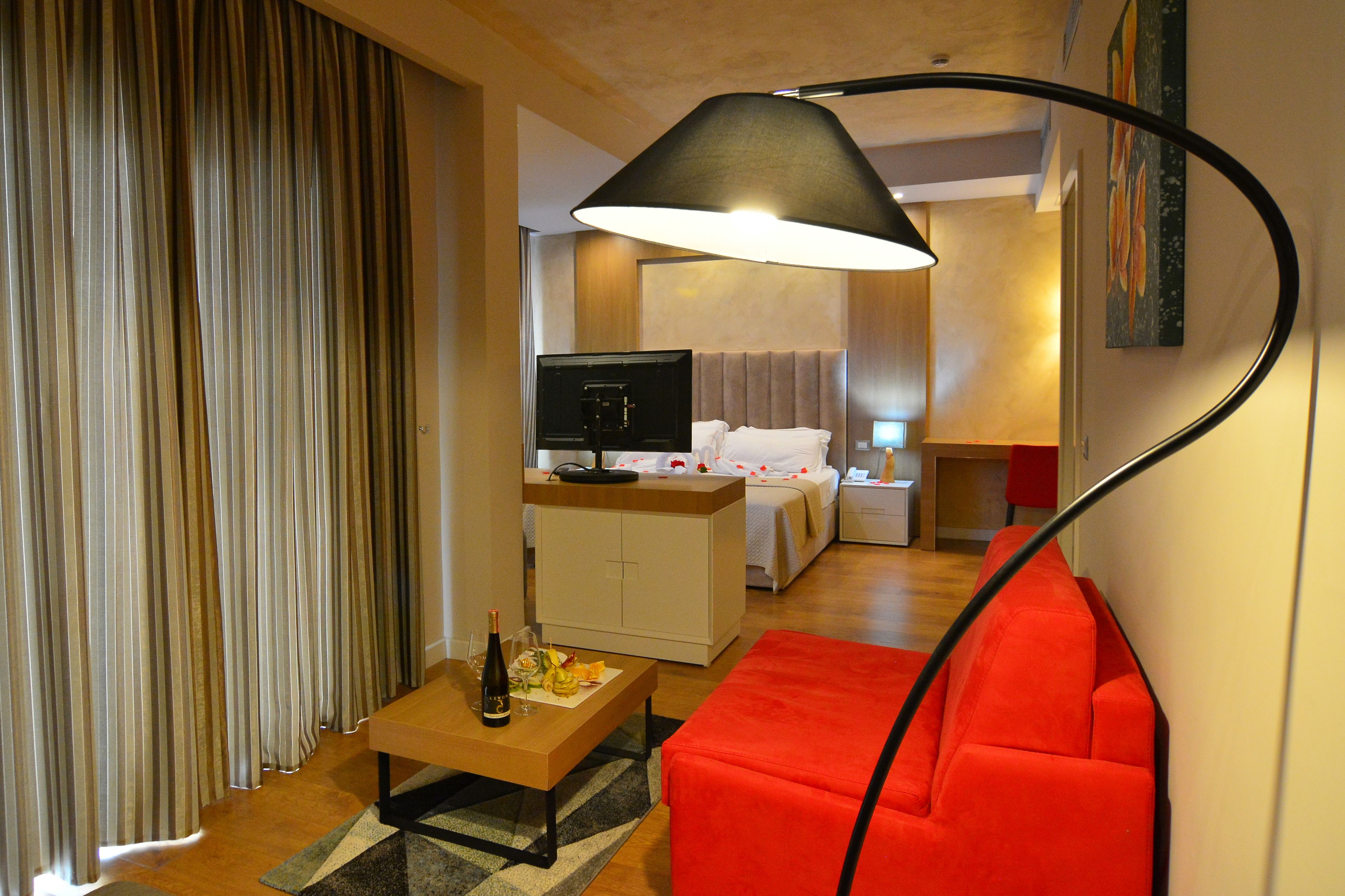 Et hotelværelse med en seng, et skrivebord, en rød sofa, et fjernsyn og en lampe.