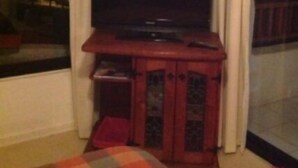 A room with a television on a wooden cabinet, a window with curtains, and a checkered rug on the floor. - Depto Maria Salas Puerto Velero (Coquimbo)