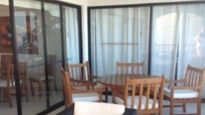 A room with a glass sliding door leading to a balcony, furnished with wooden chairs and a black sofa. - Depto Maria Salas Puerto Velero (Coquimbo)
