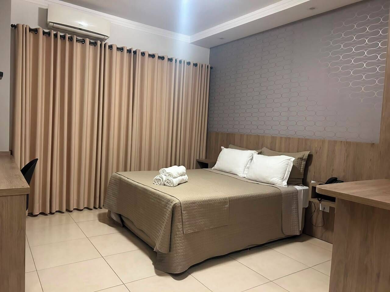A hotel room with a bed, a desk, a chair, and a wall with a textured pattern.