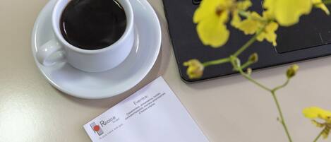 Una taza de café, una computadora portátil, un bolígrafo, una tarjeta de presentación y flores amarillas sobre una mesa.