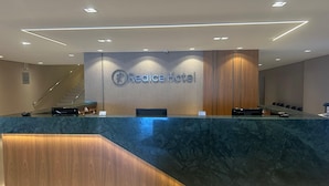 Una mesa de recepción con un letrero que dice "Realce Hotel", un dispositivo Samsung y un refrigerador Samsung.