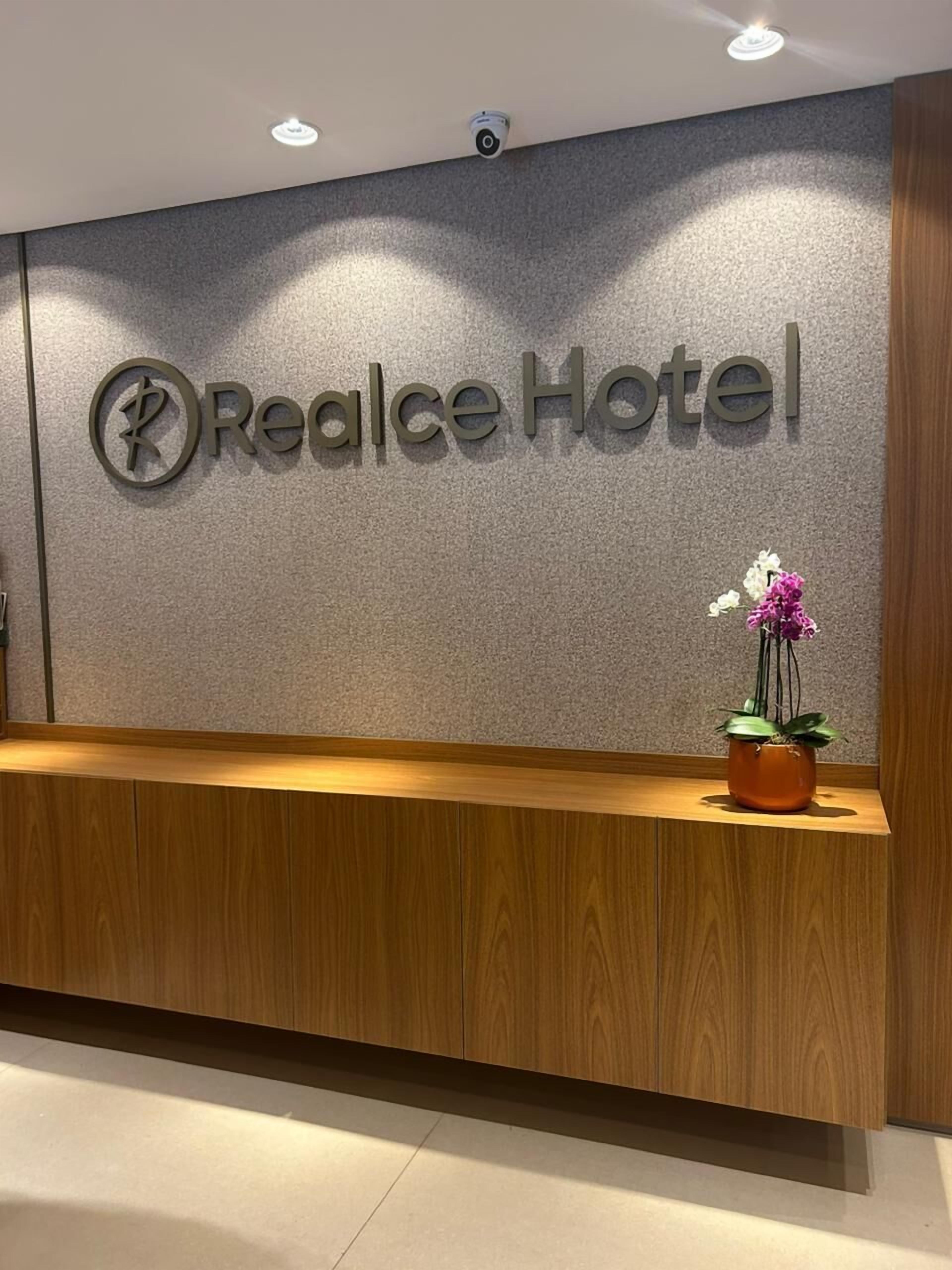 Een receptiebalie met een bord waarop 'Realce Hotel' staat en een potorkidee op de balie.