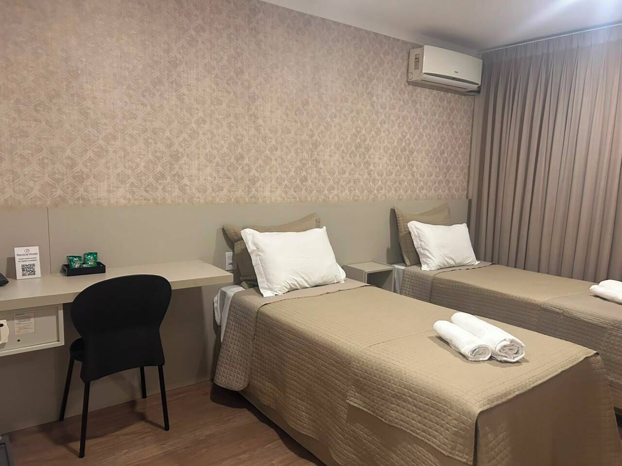 Een hotelkamer met twee bedden, een bureau, een stoel en een airconditioning.