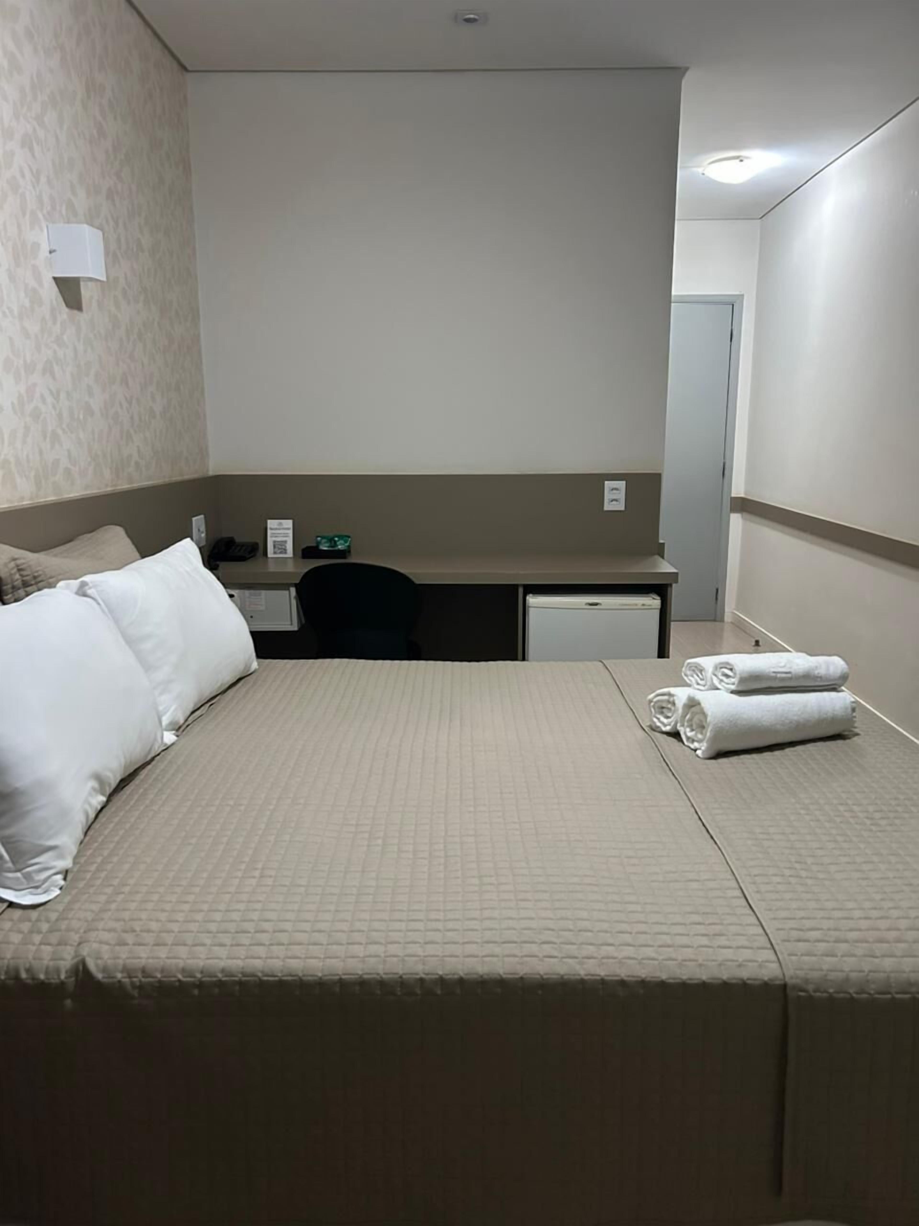 A hotel room with a bed, a desk, a chair, a phone, and a pair of towels.