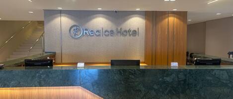 A reception desk at Realce Hotel with a modern design, a staircase in the background, and a Samsung charging station.