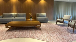 Una sala de estar moderna con una mesa de centro de madera, dos sofás grises, un sillón blanco y una pared de madera decorativa con iluminación empotrada.
