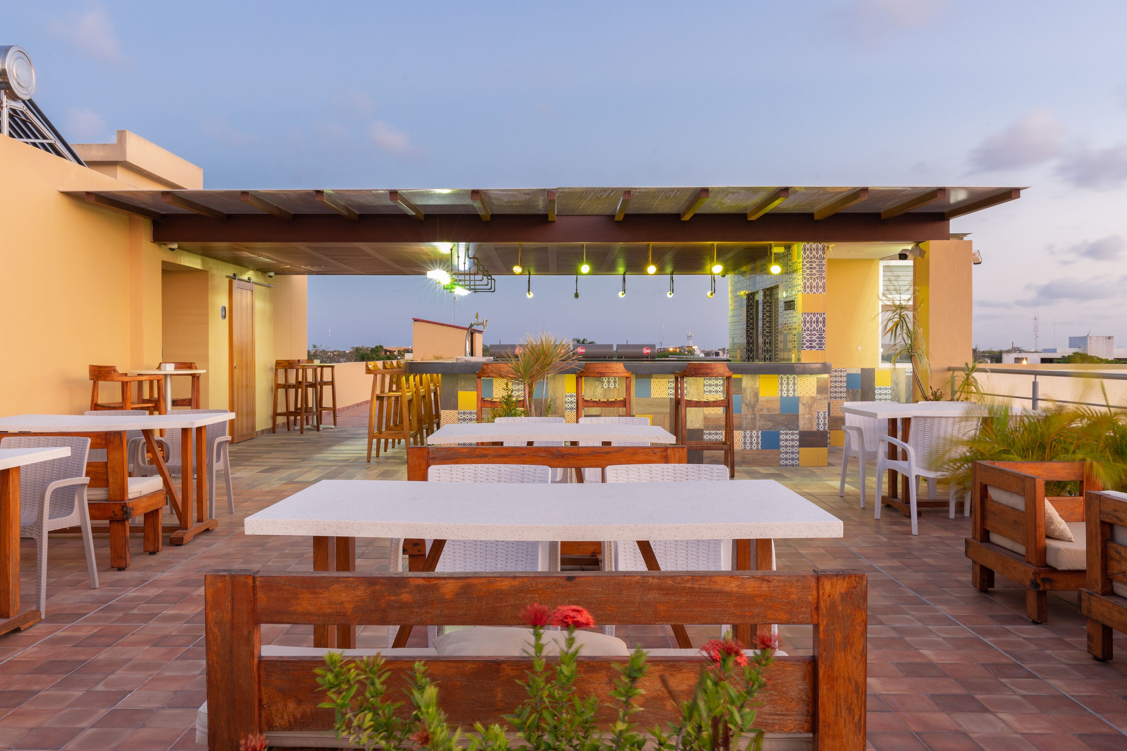 An outdoor patio with wooden tables and benches, a covered seating area, and a view of the cityscape.