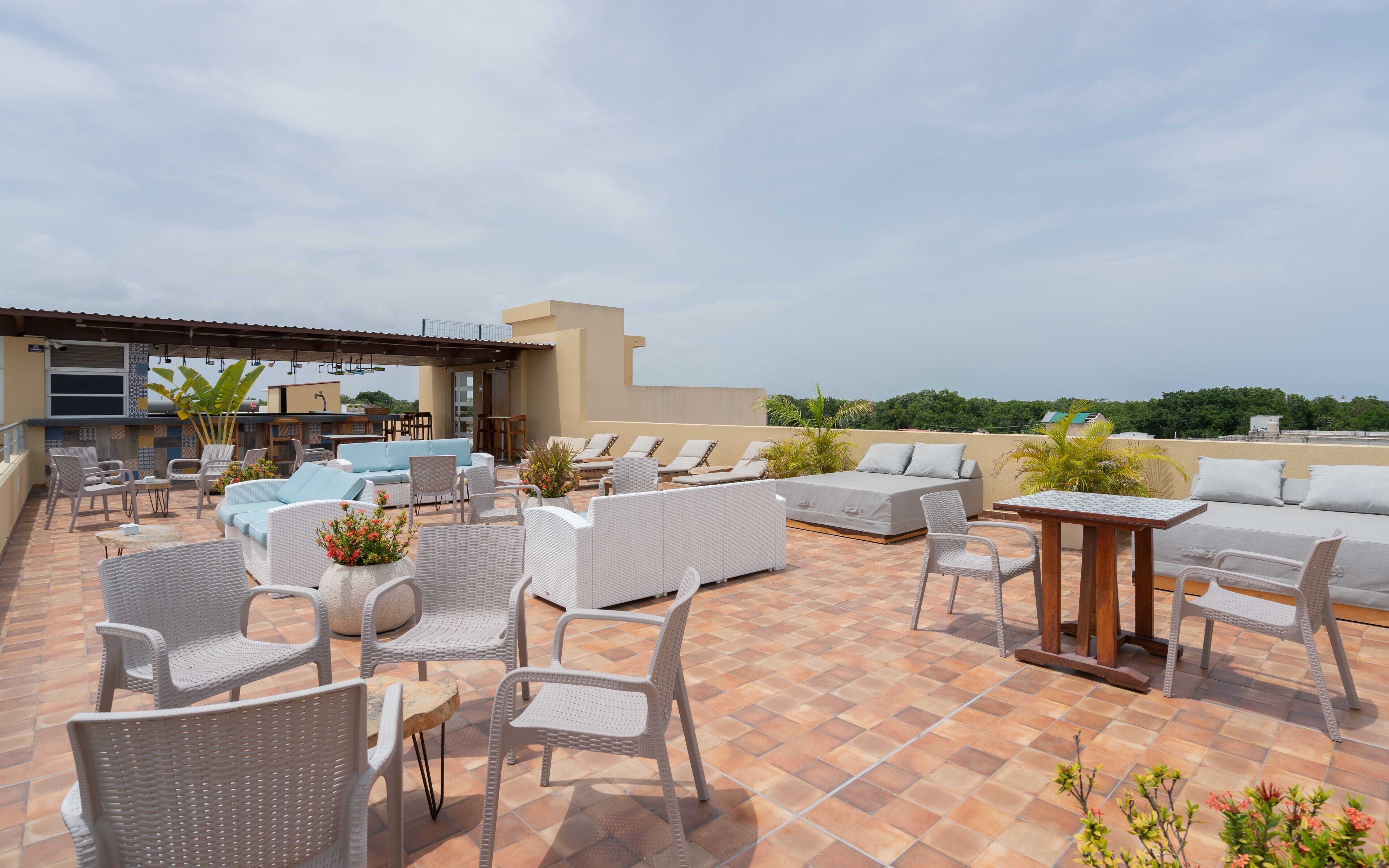 A rooftop terrace with outdoor seating, a bar area, and a view of the surrounding landscape.