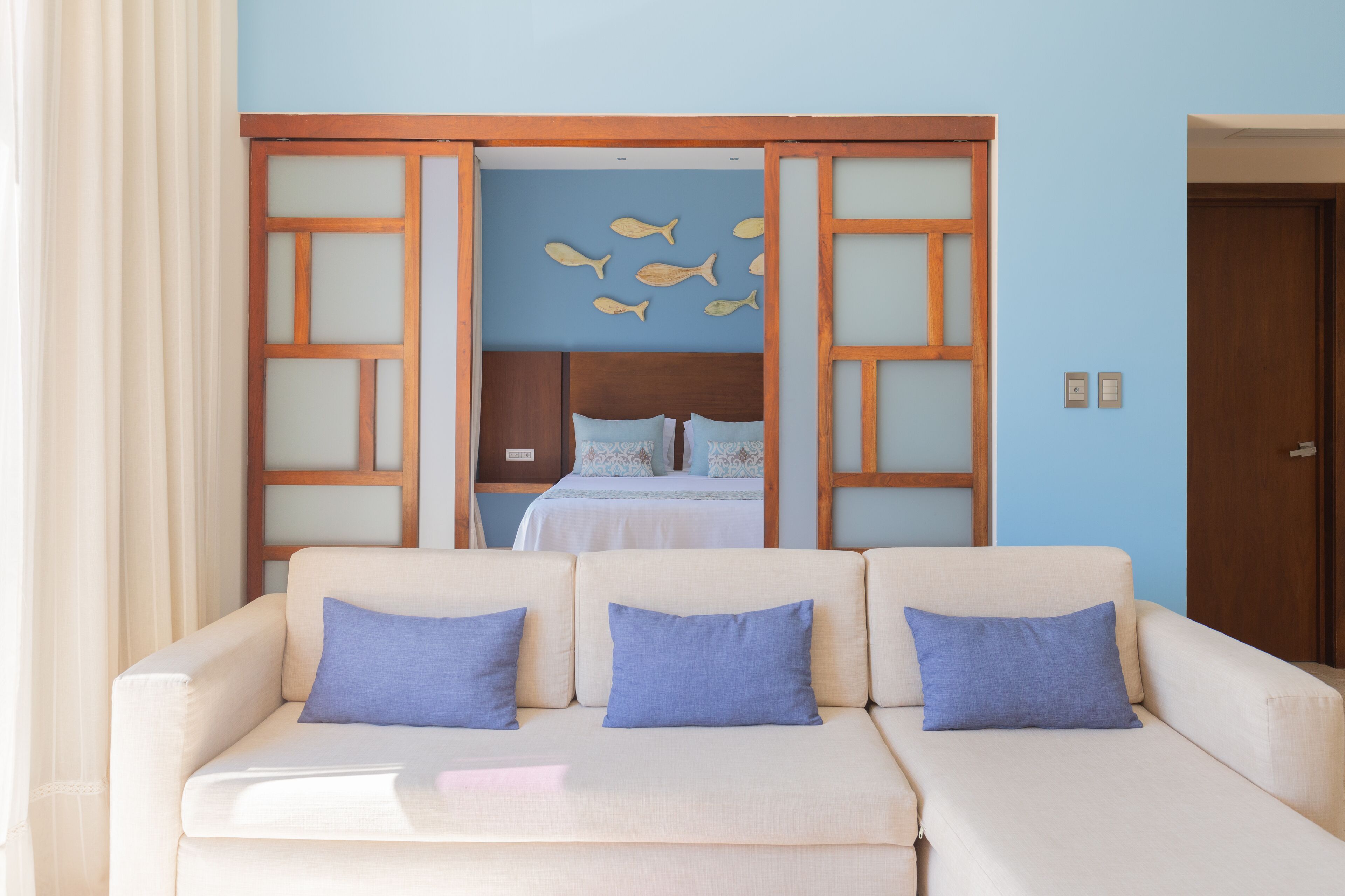 A room with a beige sofa, a bed with blue bedding, and a wall with fish decorations.