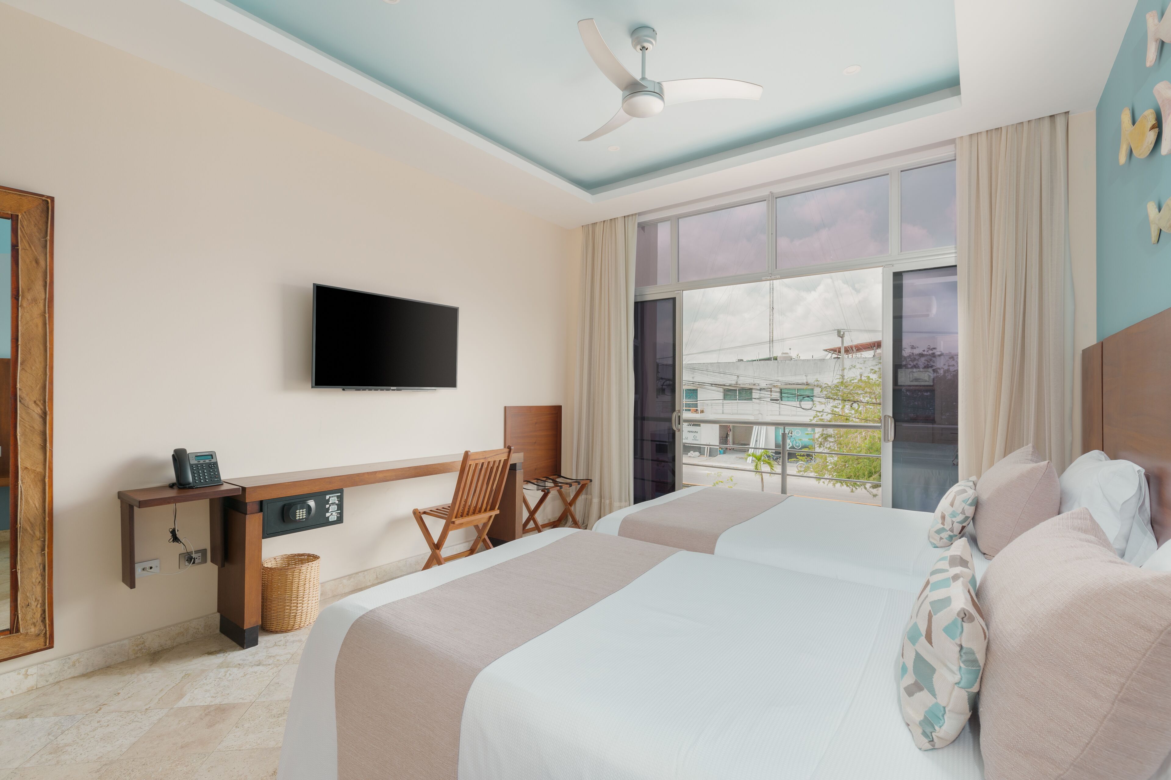 A hotel room with two beds, a desk, a chair, a television, and a large window with a view of the city.