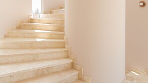 A staircase with a light-colored marble finish, leading to a landing with a large column and a window. - Biwa Tulum (Tulum)