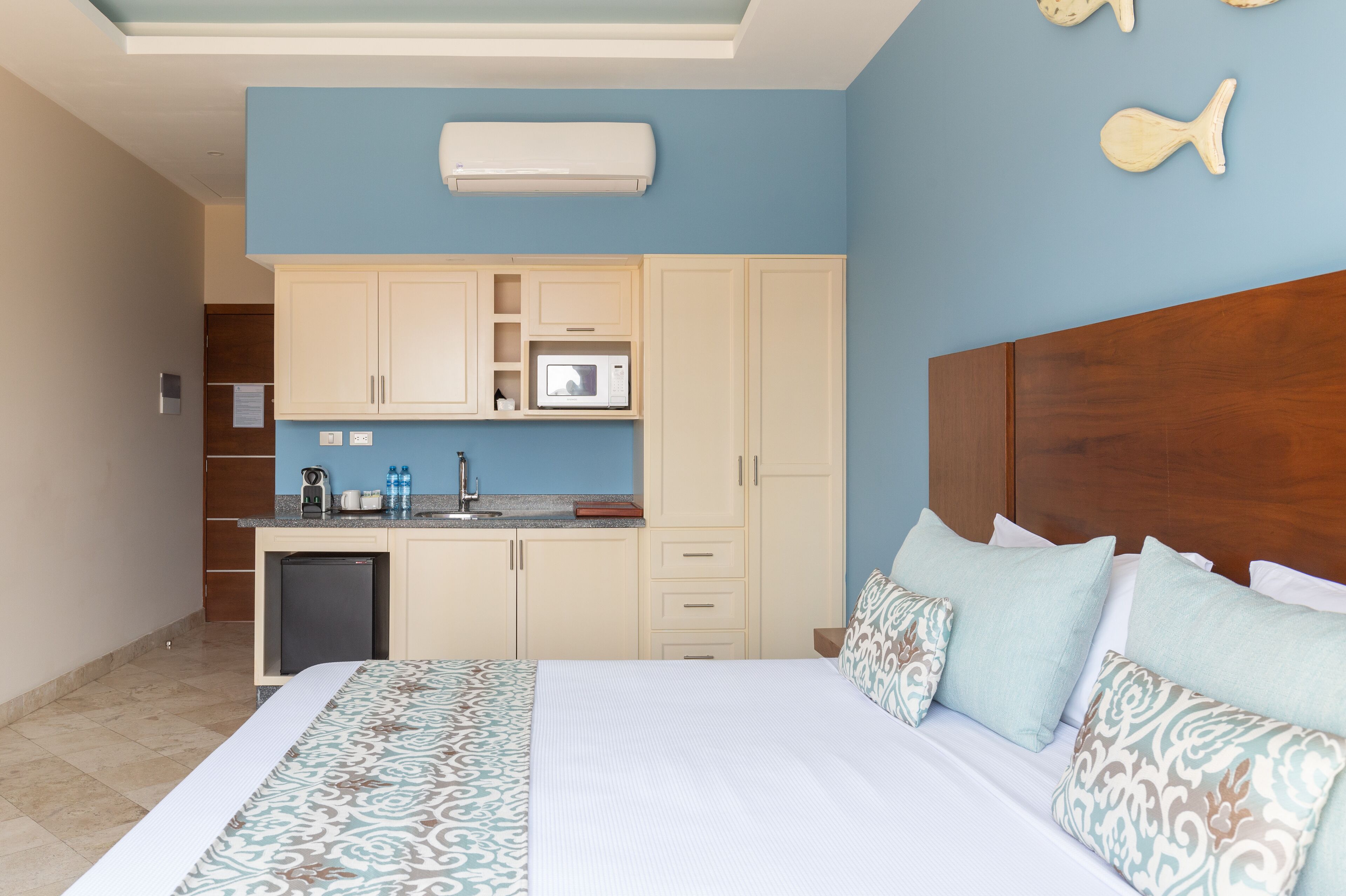 Une chambre d’hôtel comprenant un lit, une tête de lit en bois, une kitchenette équipée d’un four à micro-ondes et d’un petit réfrigérateur.