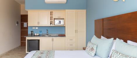 Une chambre d’hôtel comprenant un lit, une tête de lit en bois, une kitchenette équipée d’un four à micro-ondes et d’un petit réfrigérateur.