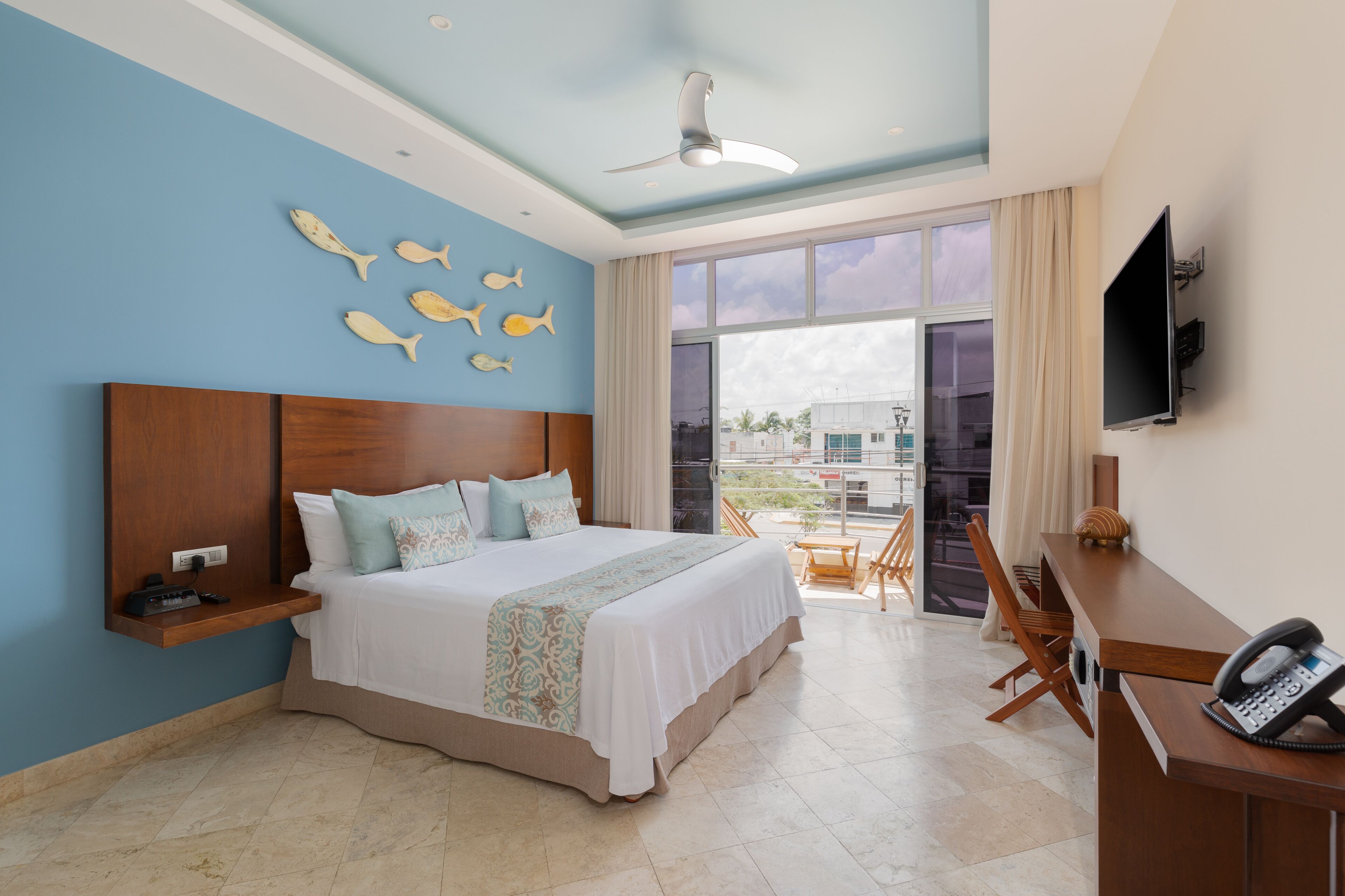 Quarto de hotel com uma cama grande, uma escrivaninha com telefone, televisão e varanda com vista.