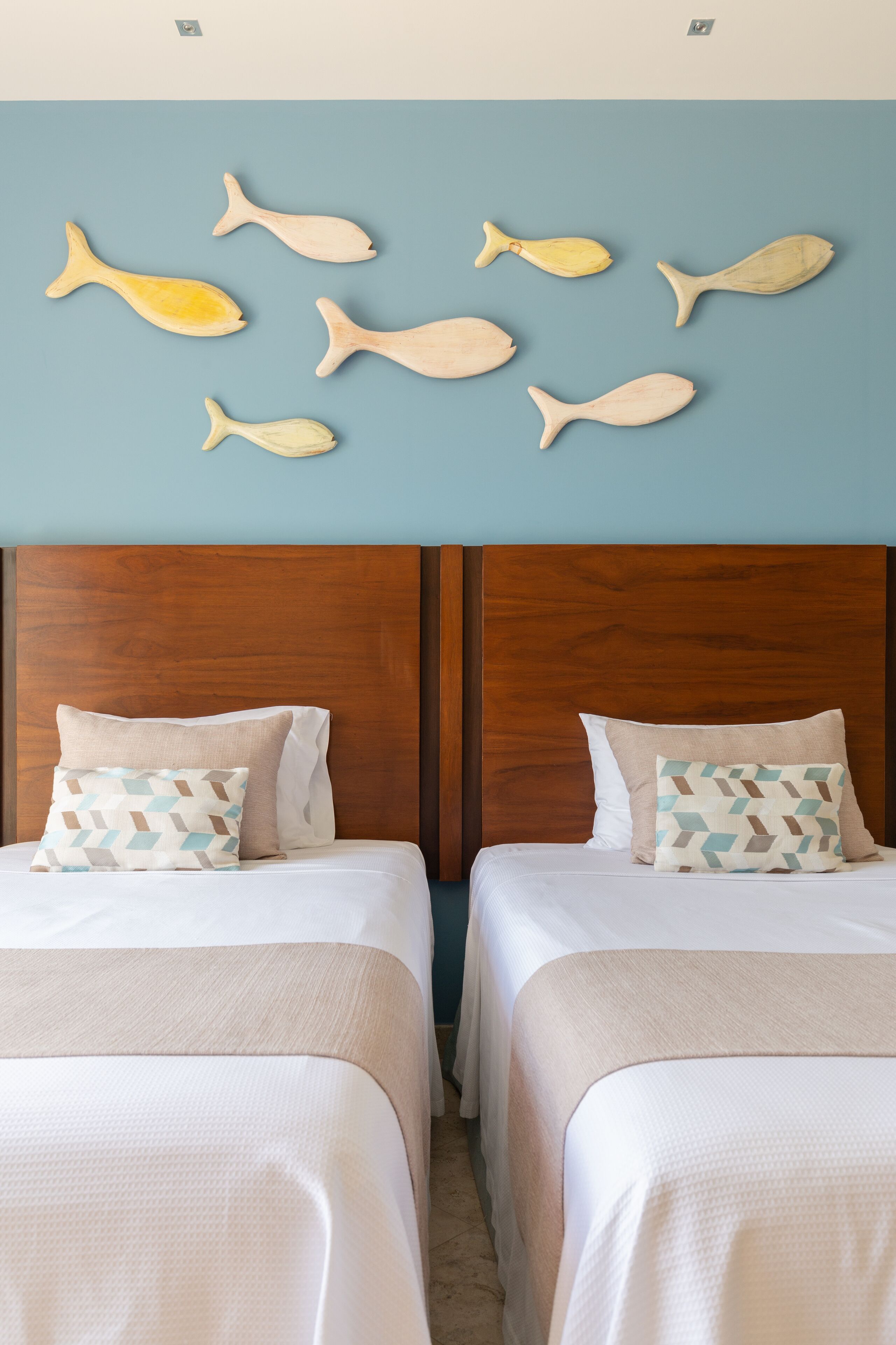 A hotel room with two beds, wooden headboards, and a wall decorated with fish-shaped wall art.