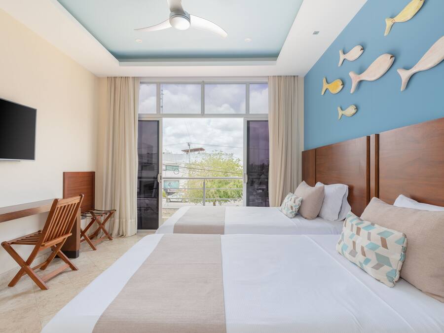Habitación de hotel con dos camas, televisión de pantalla plana, ventilador de techo y un ventanal con vistas al exterior.