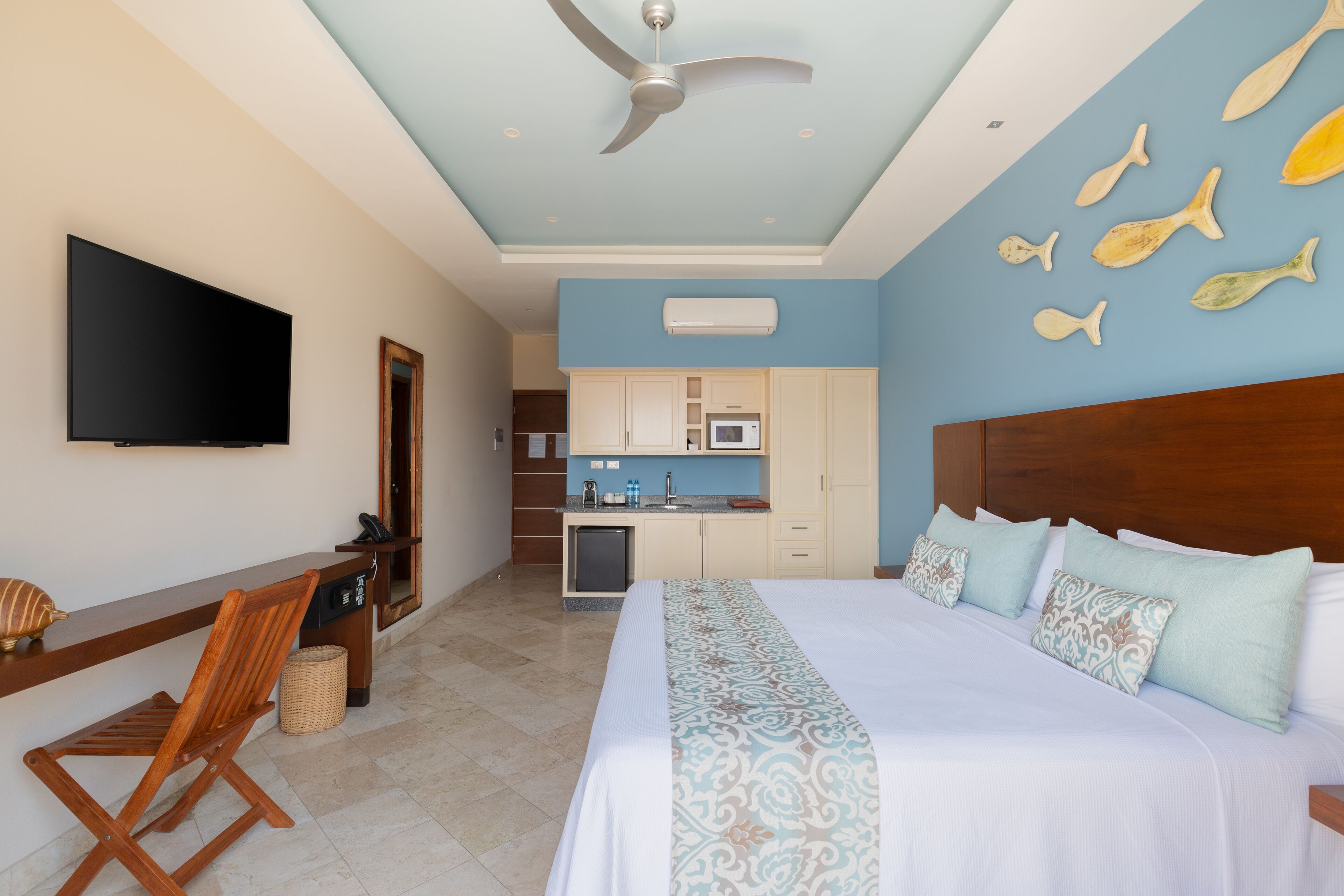 A hotel room with a bed, a desk, a chair, a television, and a kitchenette.