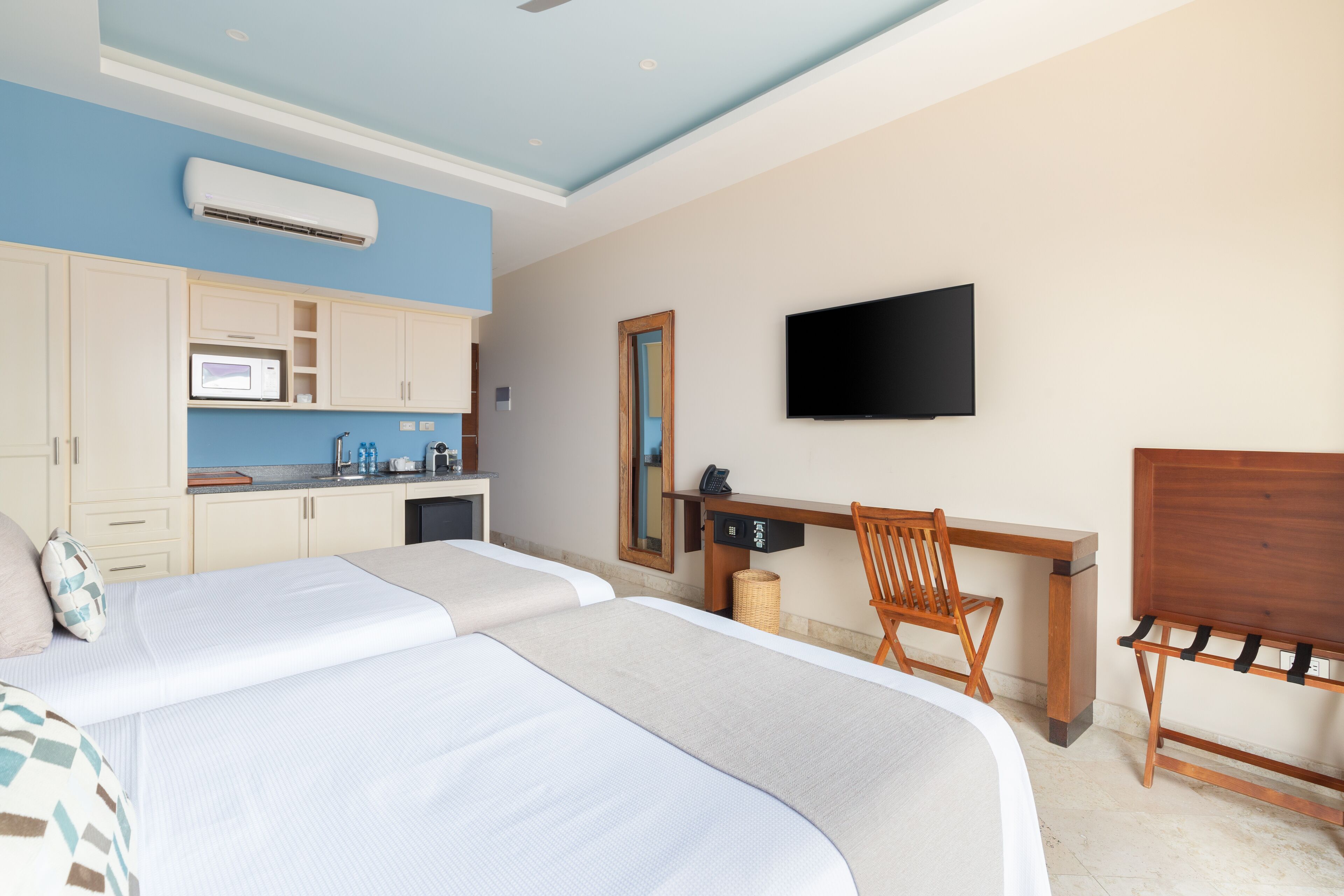Ett hotellrum med två sängar, ett skrivbord, en stol, en TV och ett litet kök.