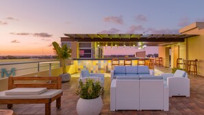 A rooftop terrace with outdoor seating, a bar area, and a view of the city skyline at sunset. - Biwa Tulum (Tulum)