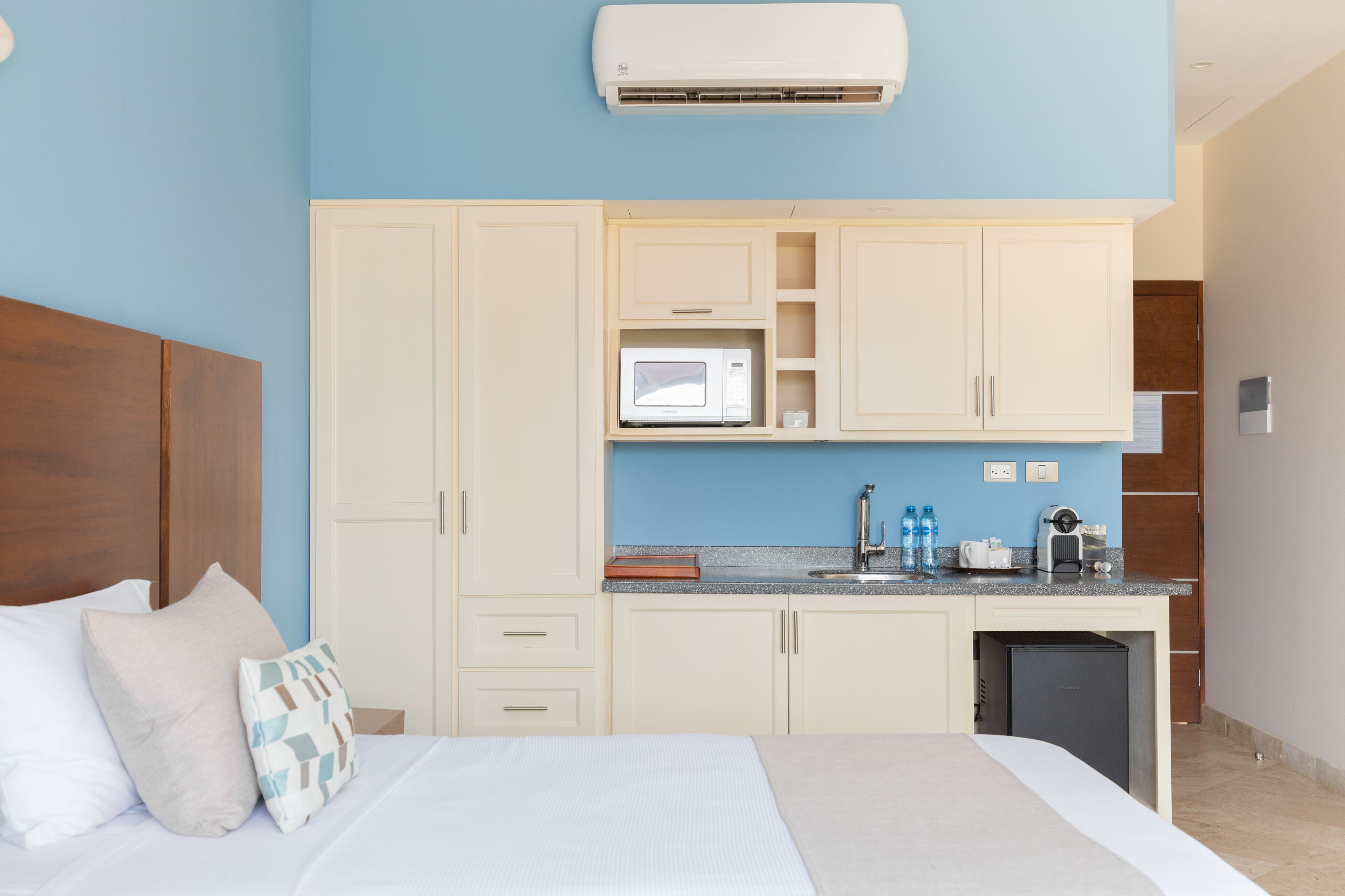 Une chambre comprenant un lit, des oreillers, une table de chevet, un bureau intégré avec un four à micro-ondes, une machine à café et un mini-réfrigérateur.