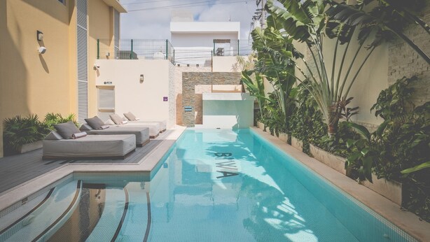 A swimming pool with a clear blue water, surrounded by a modern building with a balcony and a garden area with plants. - Biwa Tulum (Tulum)