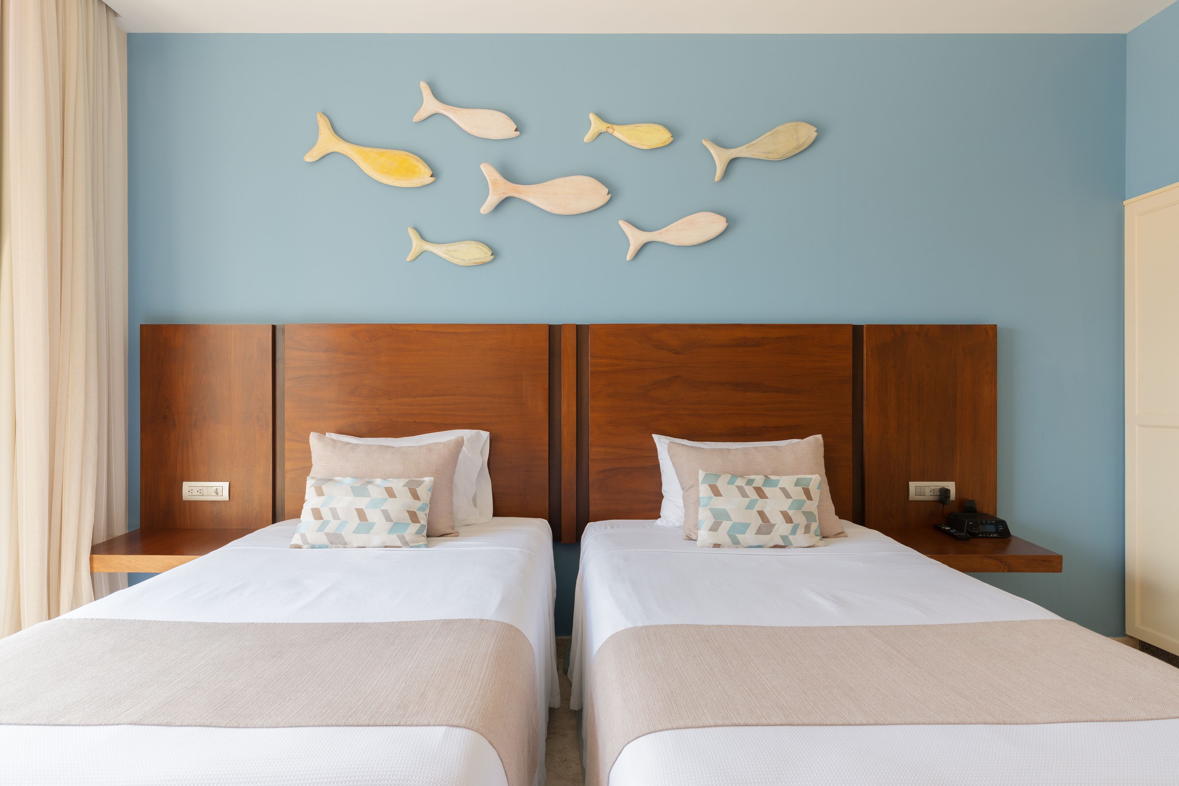 A hotel room with two beds, wooden headboards, and a wall decorated with fish-shaped wall art.