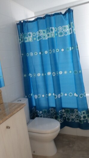 A bathroom with a white toilet, a blue shower curtain with circular patterns, and a beige countertop.