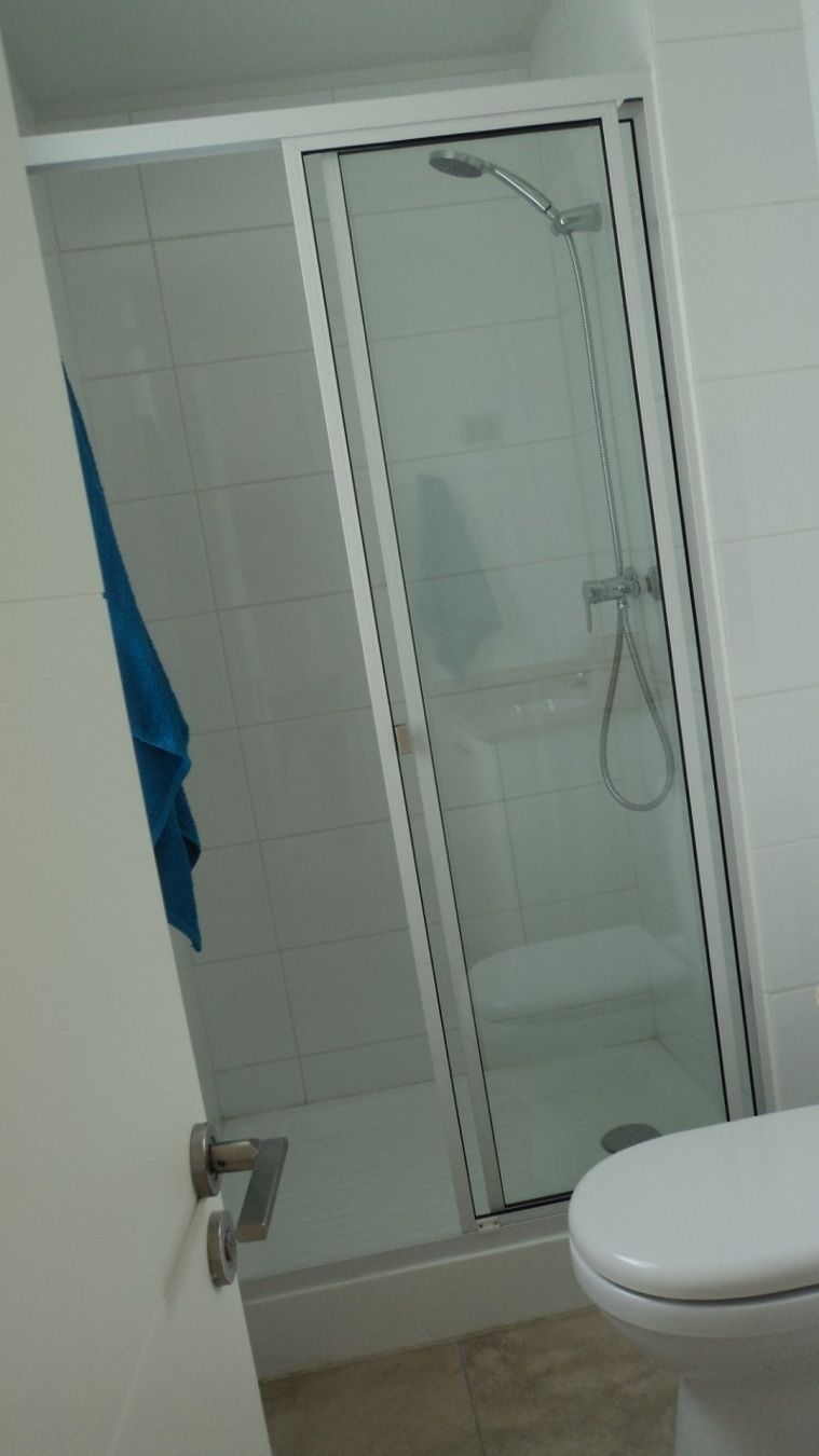 Kylpyhuoneessa on lasiseinällä varustettu suihku, valkoinen wc-istuin ja seinälle ripustettu sininen pyyhe.