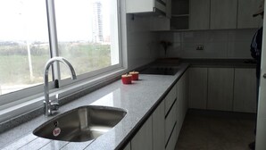 A modern kitchen with a stainless steel sink, a window with a view of buildings, and a countertop with a red container. - Depto Claudia Peñuelas (Coquimbo)
