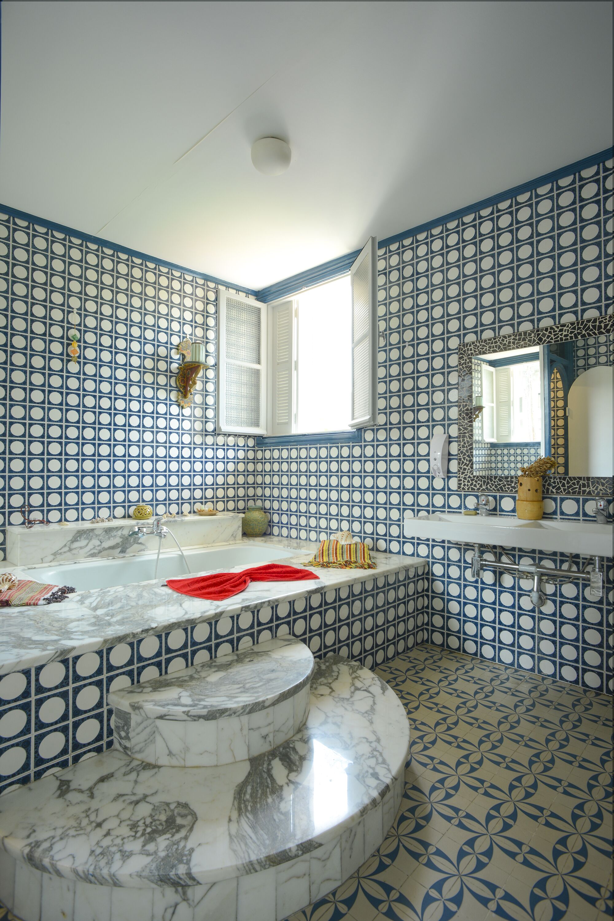 Een badkamer met een bad, een wastafel en een spiegel. De wanden zijn betegeld met een blauw-wit patroon.