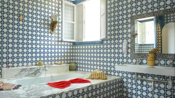 Een badkamer met een bad, een wastafel en een spiegel. De wanden zijn betegeld met een blauw-wit patroon.