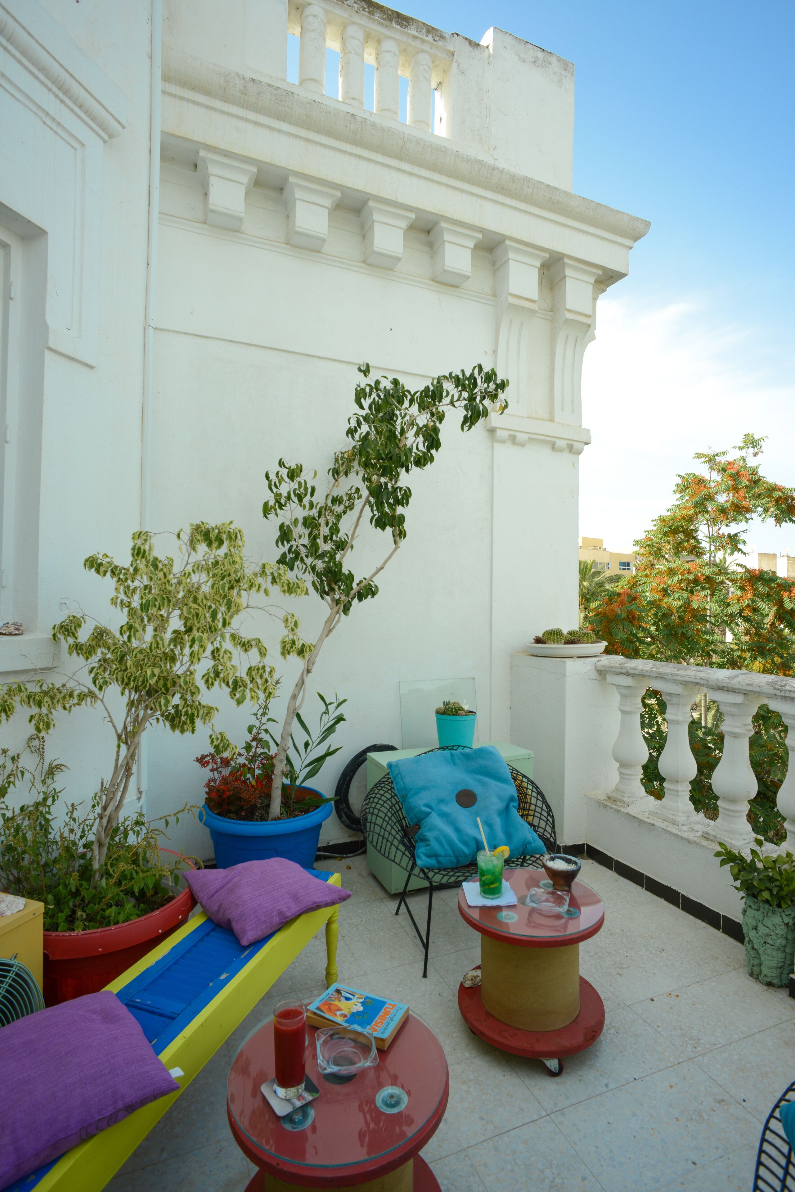 Une terrasse sur le toit avec un banc jaune et bleu, une petite table avec des boissons et des plantes en pot.