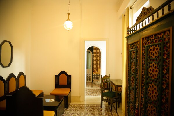 Una habitación tradicional con cama, una mesa y una silla. Se observa una puerta con diseños intrincados y un suelo con estampado.