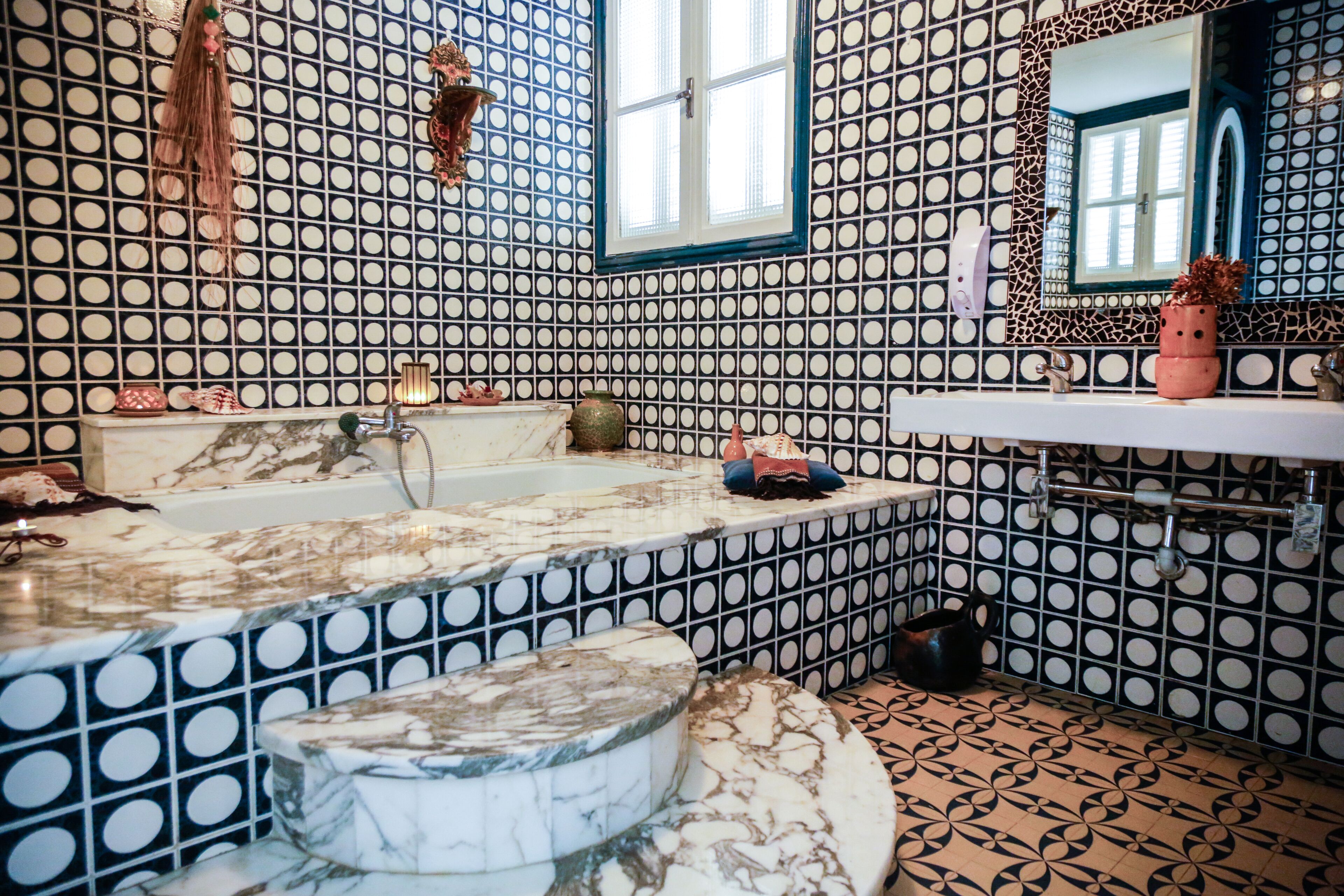 Une salle de bain avec un carrelage à motifs de pois noirs et blancs, une baignoire en marbre et un lavabo surmonté d’un miroir.