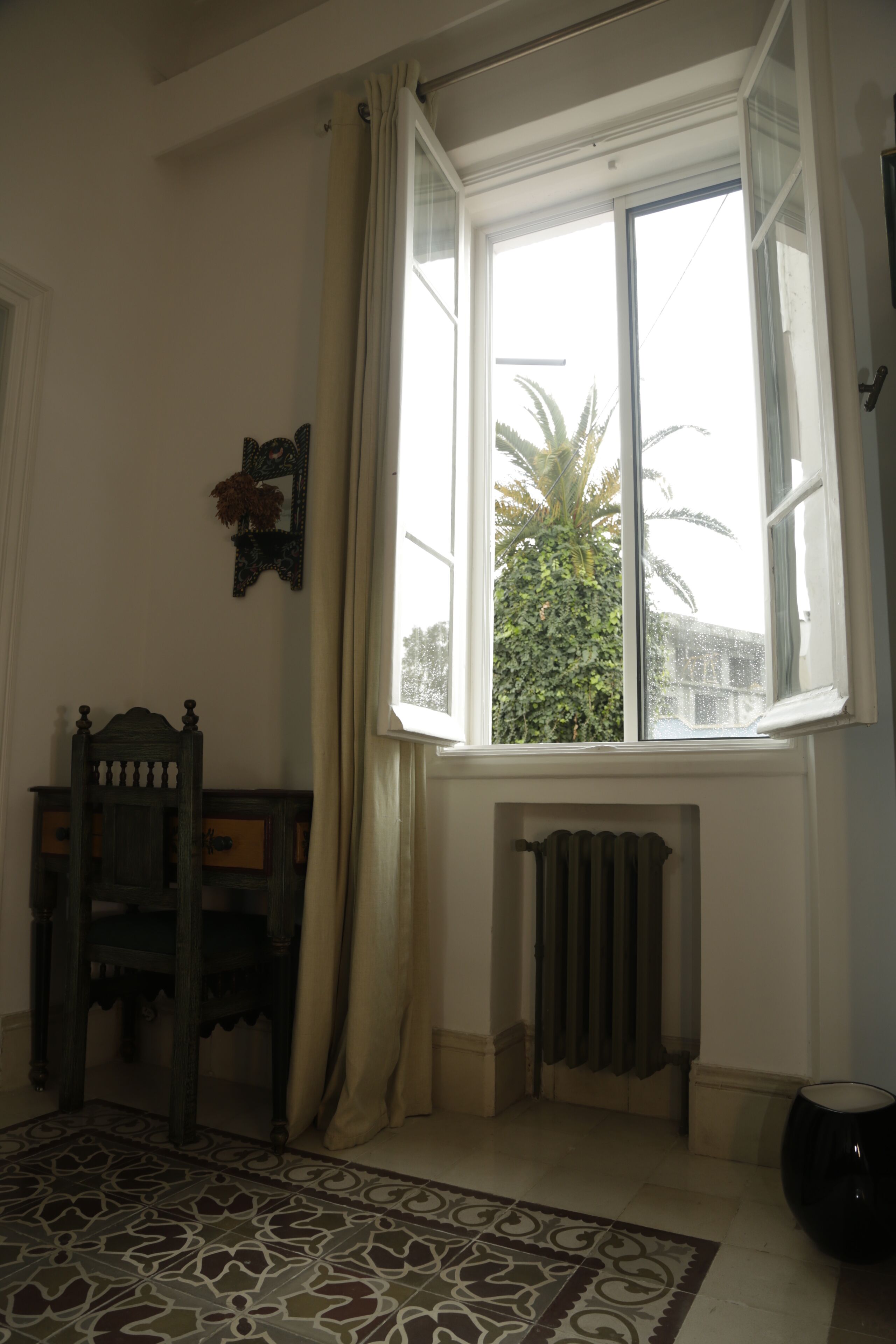 A room with a large window, a radiator, a patterned rug, and a wooden chair.