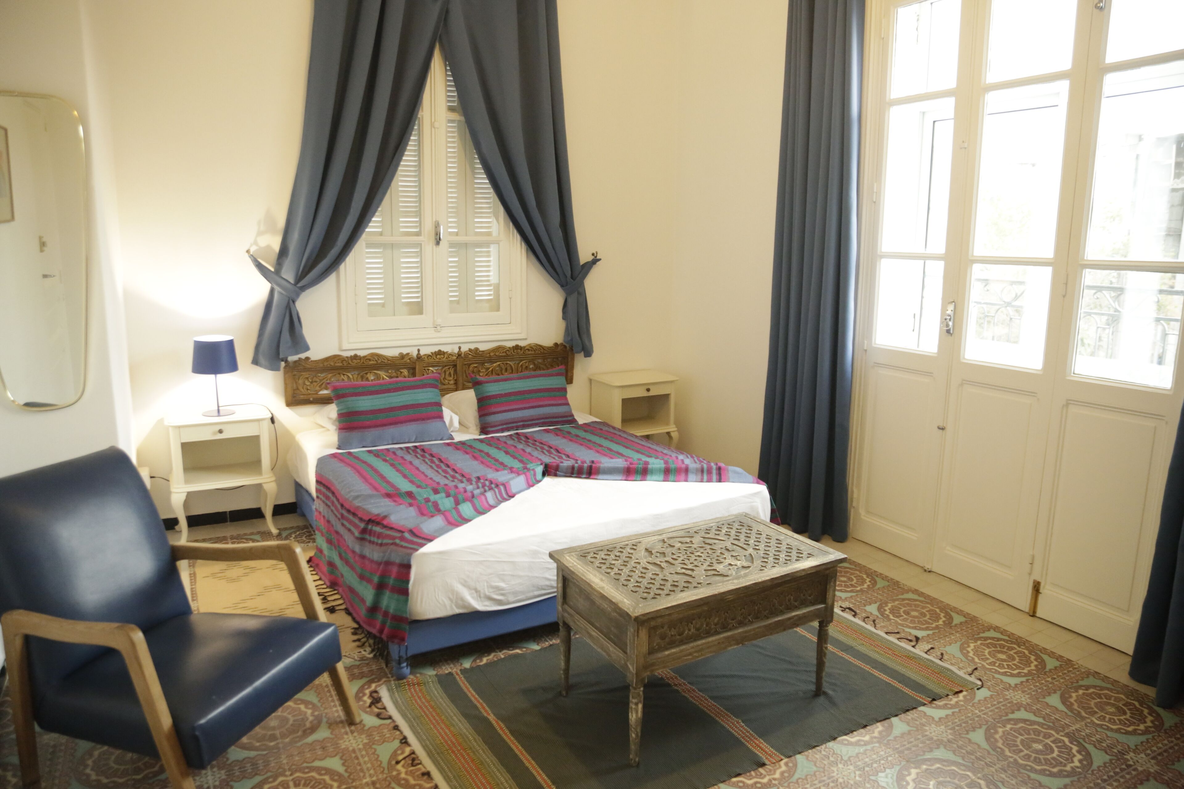 A bedroom with a bed, a chair, a nightstand, a lamp, and a window with curtains.