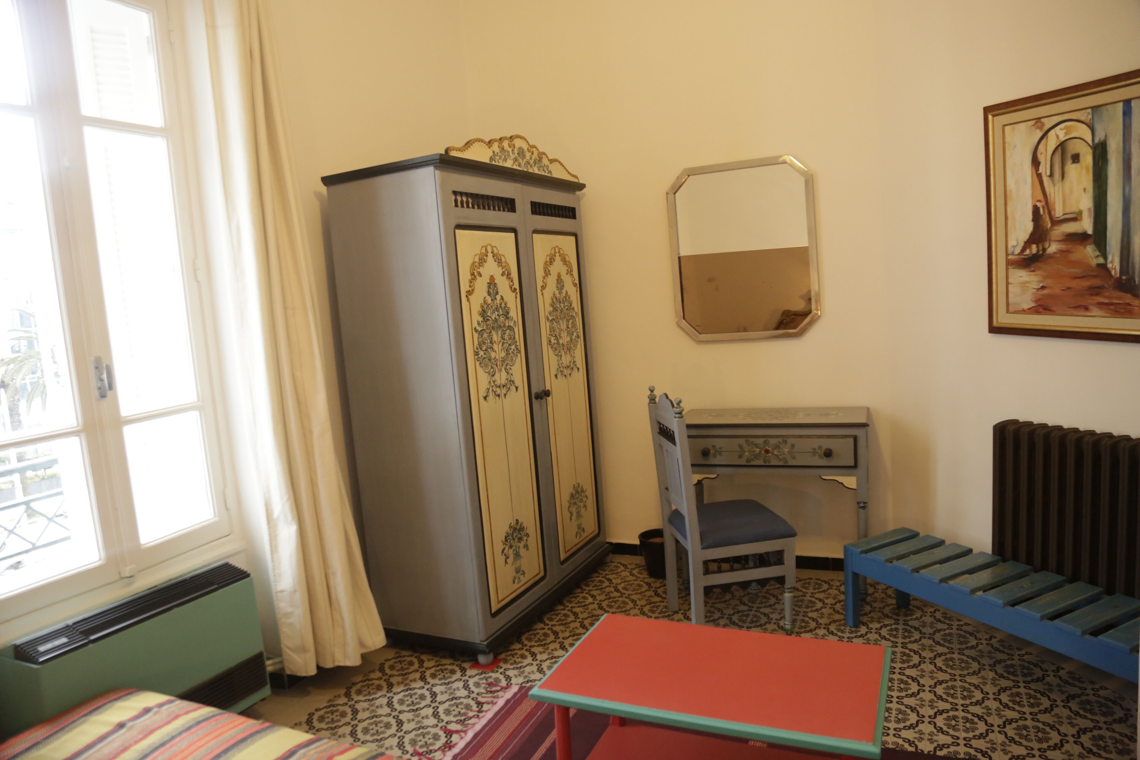 Een kamer met een bed, een bureau, een kledingkast, een radiator en een raam met gordijnen.