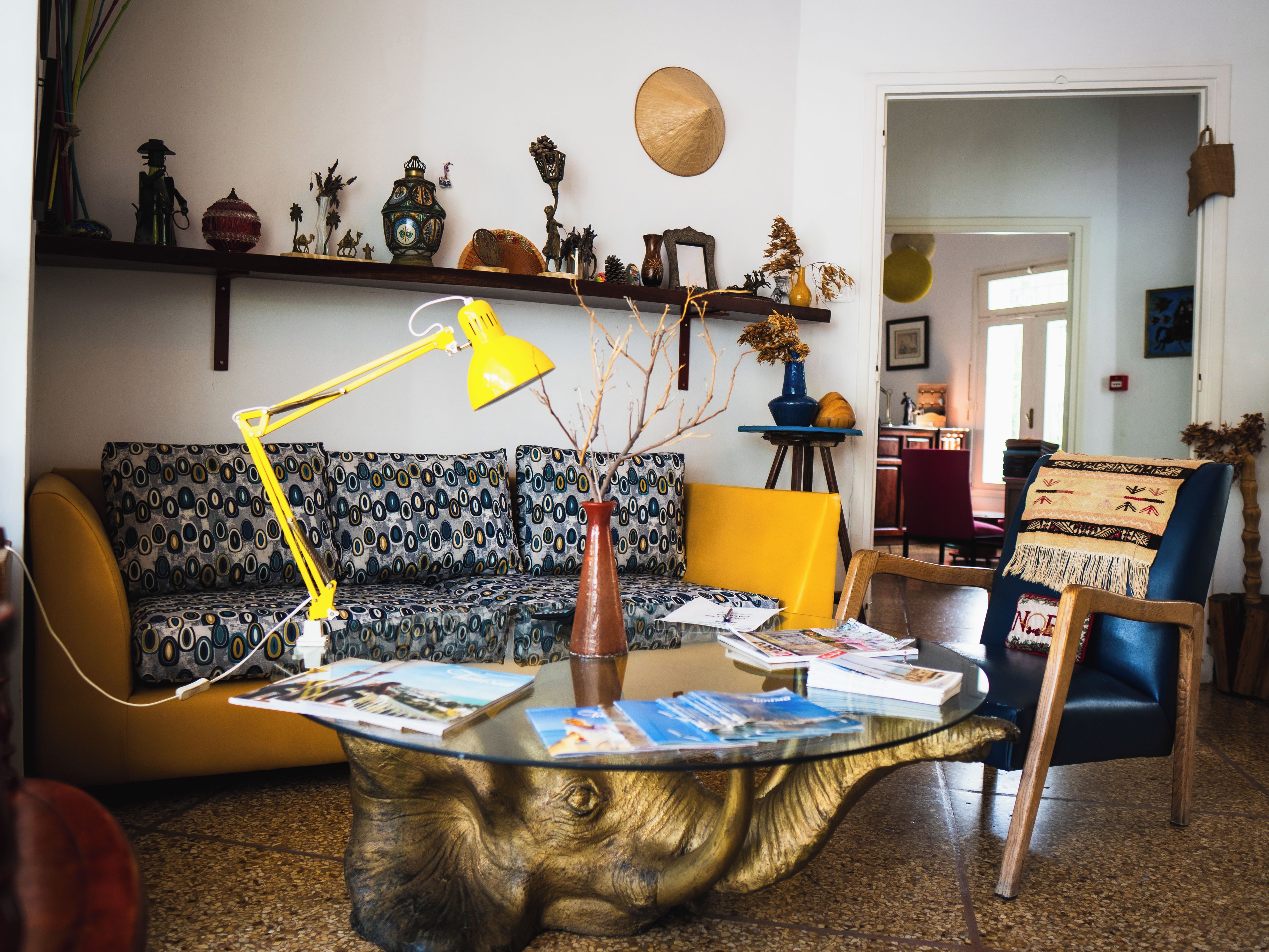 Un salon avec un canapé à motifs, une table basse ronde en verre et une lampe jaune.