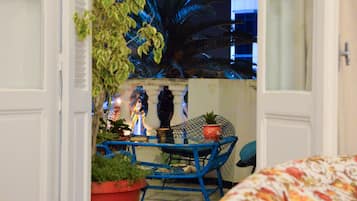 Un umbral abierto que da a un balcón con planta en maceta, una silla y una mesa.